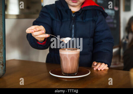 Midsection of boy holding frothy drink in spoon at cafe Stock Photo
