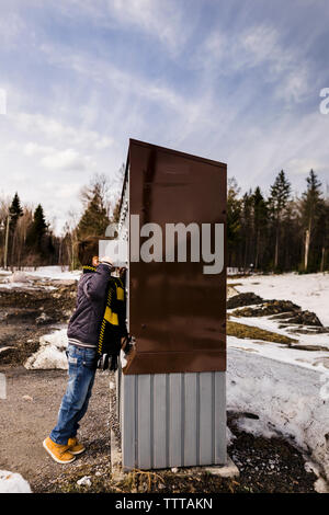 Side view of boy looking into public mailboxes while standing against sky during winter Stock Photo