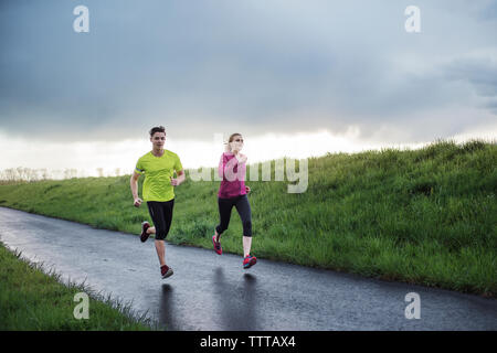 Determined athletes running on road by grassy field Stock Photo