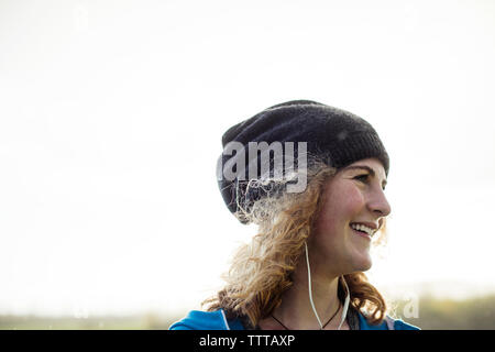 Happy female athlete listening music against clear sky