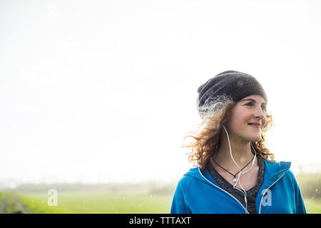 Thoughtful female athlete listening music against clear sky