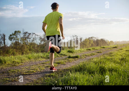 Rear view of male athlete running on field against sky Stock Photo