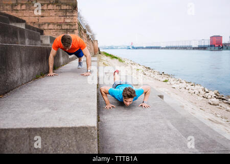 Determined male athletes doing push-ups on steps at beach Stock Photo