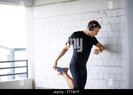 Determined man holding leg while exercising in parking lot Stock Photo