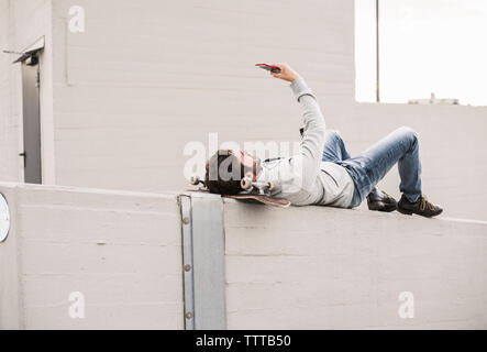 Full length of man taking selfie while lying on retaining wall Stock Photo