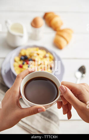 Cropped hands of woman holding coffee cup over table at home Stock Photo