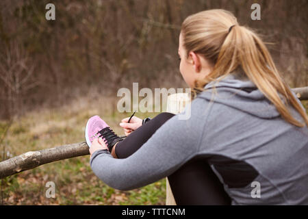 Side view of woman tying shoelace while standing at forest Stock Photo