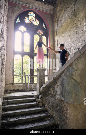 Ballerina standing on newel post while holding male friend's hand in old building Stock Photo