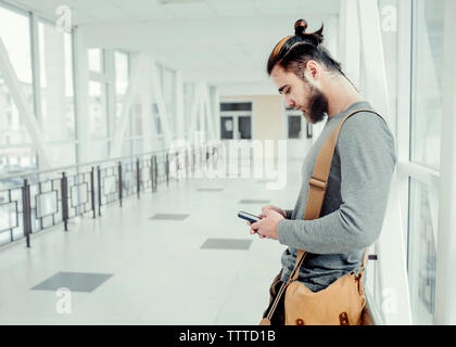 Side view of man using mobile phone while standing in corridor Stock Photo