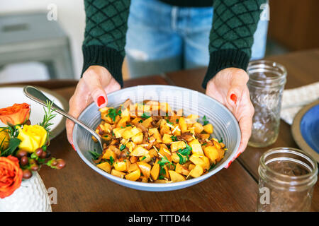 Midsection of woman holding bowl of prepared potatoes at table Stock Photo