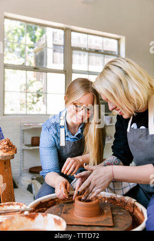 Women smiling while working on pottery wheel in workshop Stock Photo