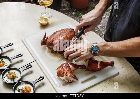 Midsection of man cutting roasted chicken on table at backyard Stock Photo