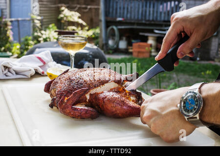 Man cutting roasted chicken on table at backyard Stock Photo