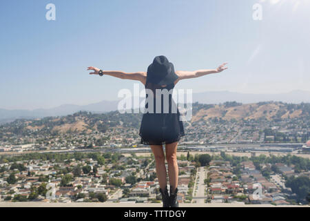 Young woman balancing on retaining wall with city in background against clear sky Stock Photo