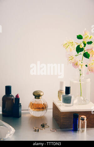 Beauty products with jewelry and flower vase on table against white wall