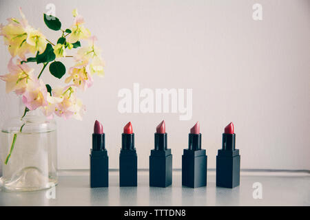 Various lipsticks arranged by bougainvillea flower vase against white wall Stock Photo