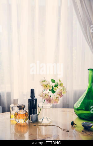 Beauty products with jewelry by flower vase on table against curtain