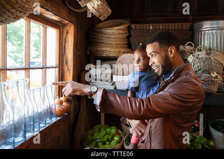 Father pointing and showing daughter while looking through window in organic shop Stock Photo