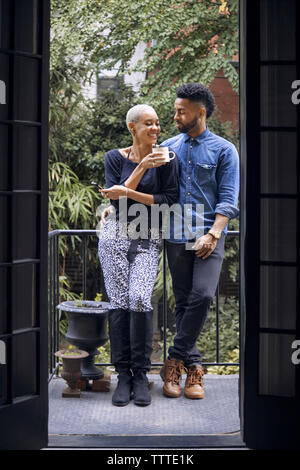 Happy couple talking while standing in balcony seen through doorway Stock Photo
