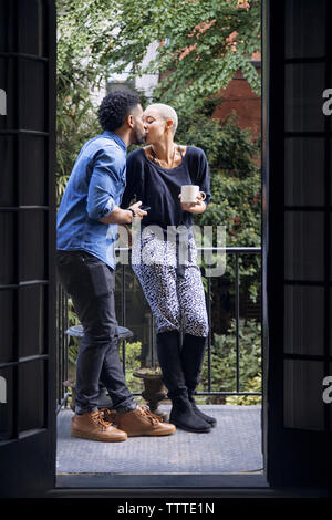 Romantic couple kissing while standing in balcony seen through doorway Stock Photo