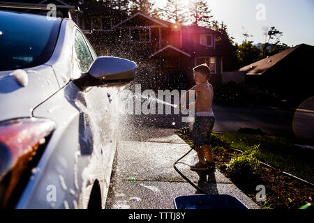 side view of boy washing car with hose Stock Photo
