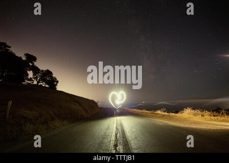 Person making heart shape while performing light painting on mountain road at night