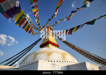 Low angle view of Boudhanath stupa with colorful prayer flags against blue sky Stock Photo