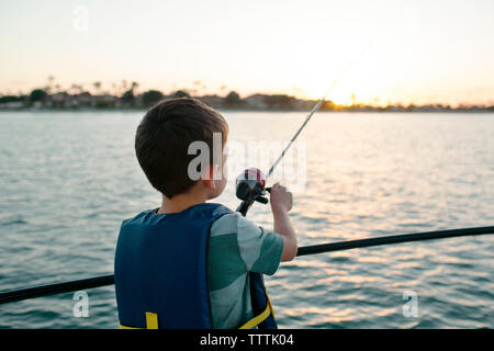 Boy fishing in sea while standing on boat Stock Photo