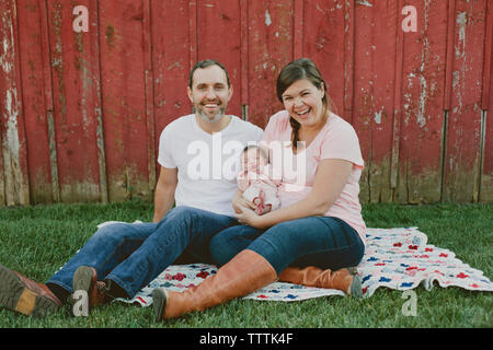 Portrait of happy mother and father with baby girl sitting on field in yard Stock Photo
