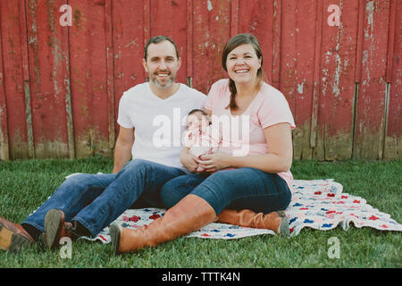 Portrait of happy parents with baby girl sitting on field in yard Stock Photo