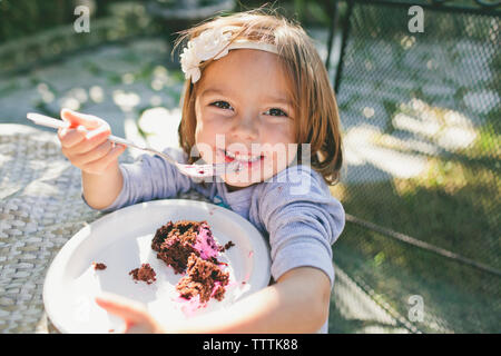 High angle portrait of cheerful girl eating birthday cake Stock Photo