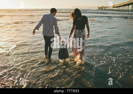 Rear view of parents holding daughter's hands while walking in sea Stock Photo