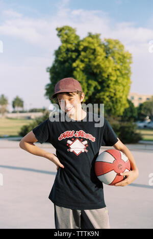 Portrait of happy boy holding basketball while standing on footpath Stock Photo