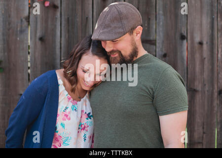 Happy couple standing against wooden fence in backyard Stock Photo