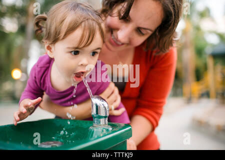 Mother helping daughter in drinking water from fountain Stock Photo