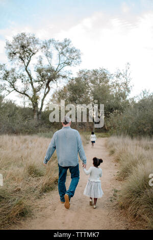 Rear view of father and daughters walking on field at park Stock Photo