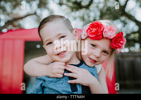 Portrait of cute siblings standing against red garage in yard Stock Photo