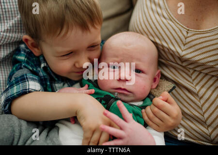 Cute boy carrying newborn brother while sitting between parents at home Stock Photo