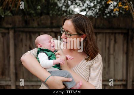 Mother carrying crying newborn son while standing in park Stock Photo