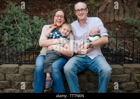 Portrait of happy family with newborn sleeping baby boy sitting in park Stock Photo