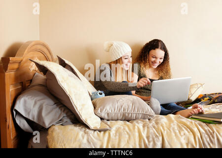 Happy friends using laptop computer while sitting on bed at home Stock Photo