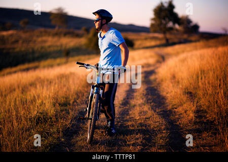 Full length of male cyclist standing with bicycle on dirt road field Stock Photo