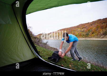 Man opening backpack by river Stock Photo