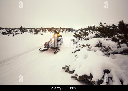 Man driving snowmobile on snowy field against sky Stock Photo