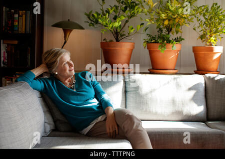 Thoughtful woman sitting on sofa at home Stock Photo