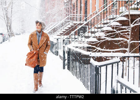 Woman looking away while walking on snow covered field during snowing Stock Photo