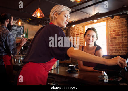 Woman looking at owner using machine at cash counter Stock Photo