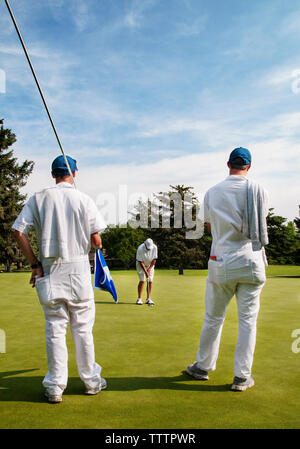 Rear view of caddies looking at golfer taking a shot in golf course Stock Photo