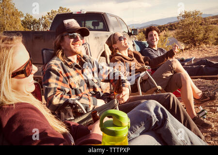 Friends enjoying while resting against off-road vehicle at campsite Stock Photo