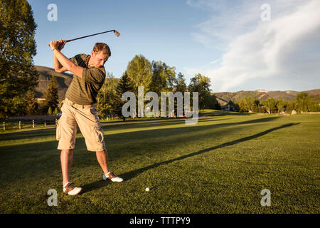 Golfer swinging golf club while standing on grassy field Stock Photo